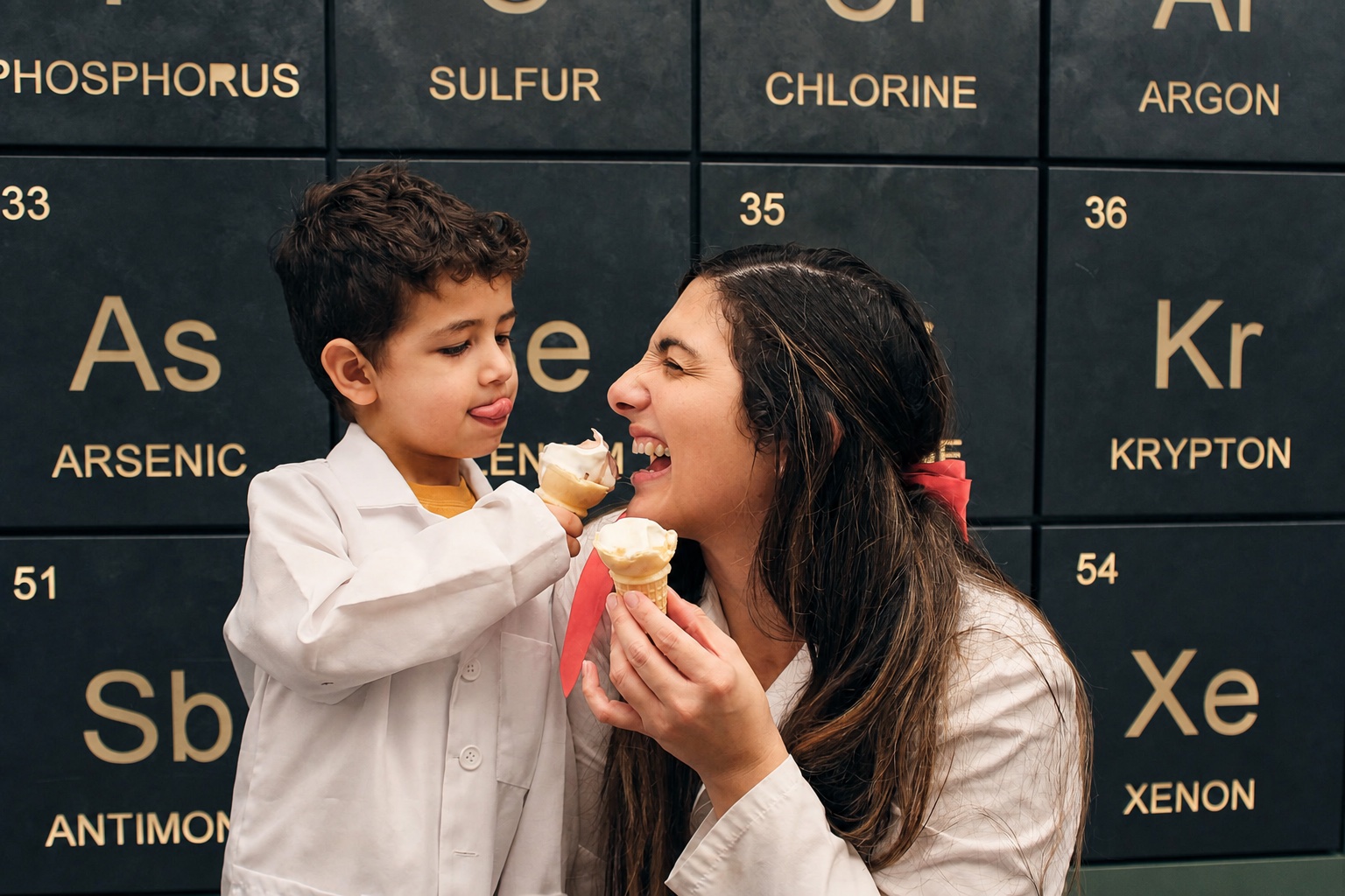 A mother and child enjoying a playful moment in front of a periodic table